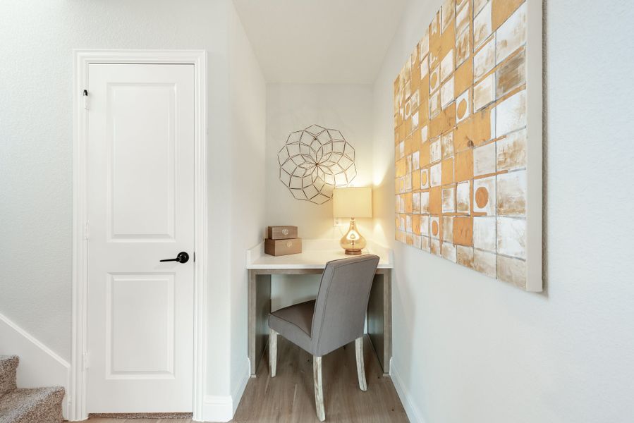 Small built-in desk nook with gray chair, lamp, and wall art on hardwood floors