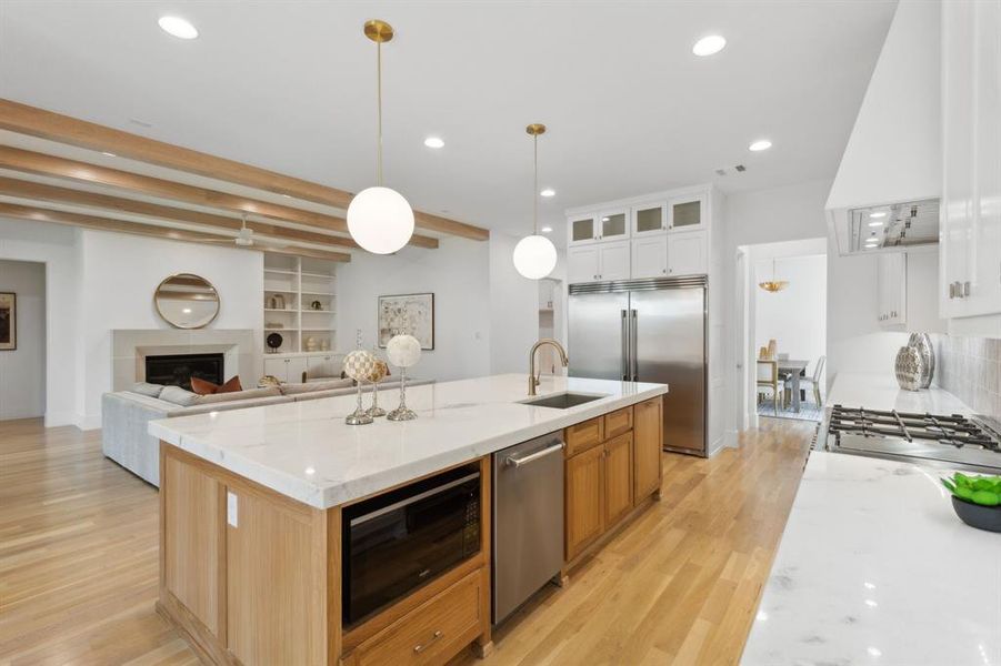 Kitchen with light stone counters, built in appliances, sink, white cabinetry, and a center island with sink