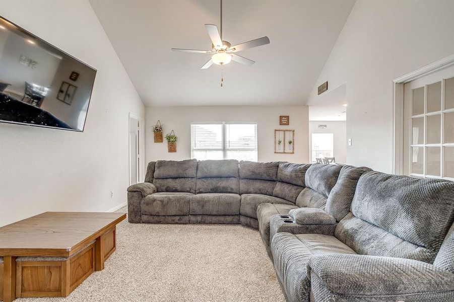 Living area with vaulted ceiling, light colored carpet, and ceiling fan