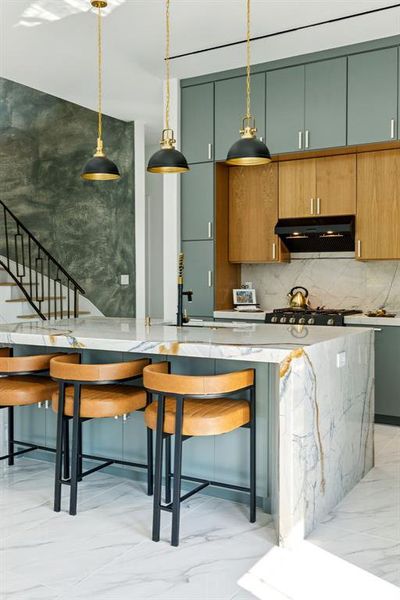 Kitchen featuring decorative backsplash, light marble finish flooring, decorative light fixtures, brown cabinetry, and light stone countertops Kitchen featuring decorative backsplash, light marble finish flooring, decorative light fixtures, brown cabinetry, and light stone countertops