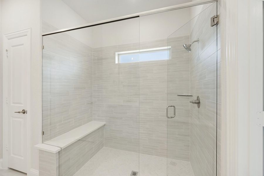 Walk-in shower with gray tile walls, glass door, built-in bench, and small window