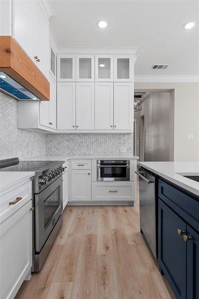 Kitchen featuring backsplash, light hardwood / wood-style floors, stainless steel appliances, and white cabinets