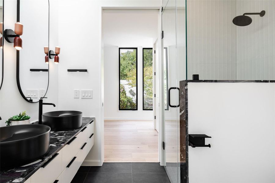 Full bath with double vanity, dark tile patterned flooring, and a tile shower