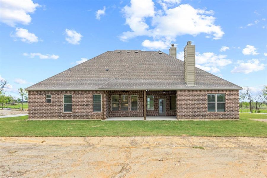 Brick exterior with a covered patio, multiple windows, and a shingle roof
