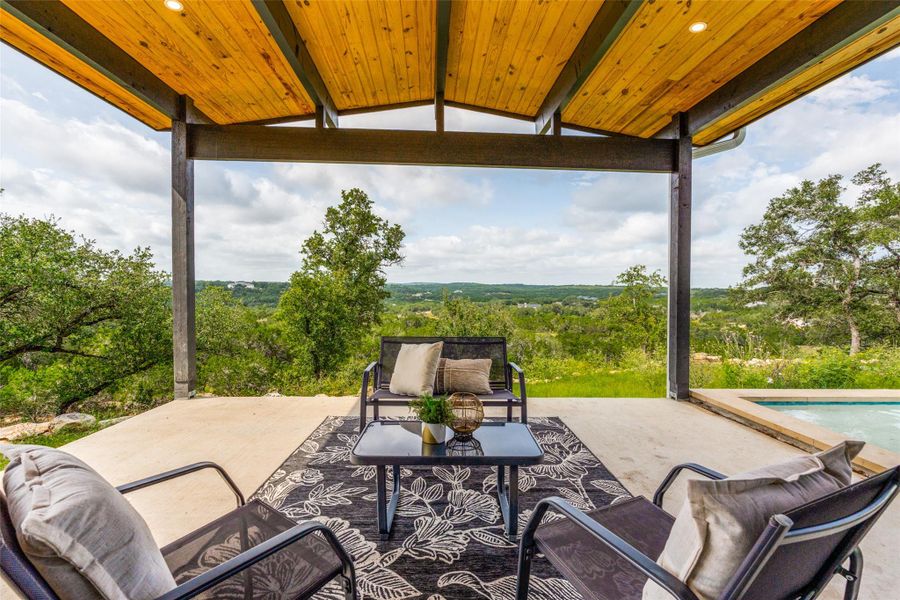 An inviting covered patio with a ceiling fan overlooks a private pool and scenic natural views.