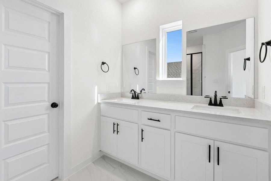 Full bathroom featuring double vanity, a stall shower, and light marble finish flooring