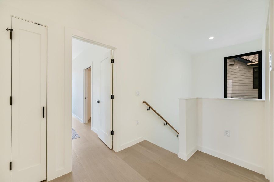 Hallway with an upstairs landing, light wood-style floors, and recessed lighting