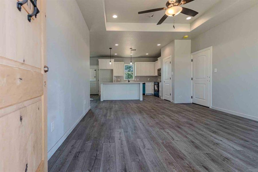 Unfurnished living room with dark wood-style flooring, recessed lighting, a tray ceiling, and a ceiling fan Unfurnished living room with dark wood-style flooring, recessed lighting, a tray ceiling, and a ceiling fan