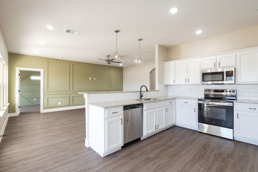 Kitchen with stainless steel appliances, backsplash, a peninsula, hanging light fixtures, and light stone counters