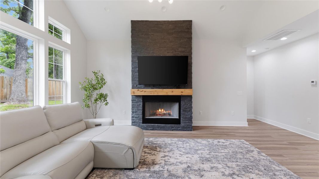 This living room has faulted ceilings, bright lighting and floor to ceiling fireplace.