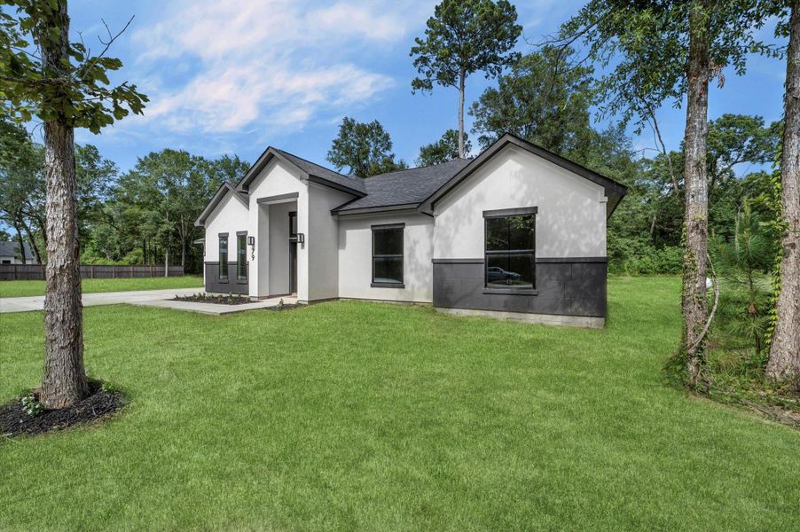 This photo shows a modern, single-story home with a sleek black and white exterior, nestled in a lush green setting with mature trees. The property features a spacious front yard and a paved driveway. This photo shows a modern, single-story home with a sleek black and white exterior, nestled in a lush green setting with mature trees. The property features a spacious front yard and a paved driveway.
