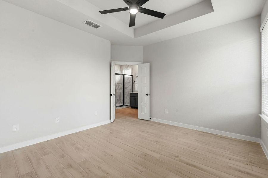 A well-lit primary bedroom features a unique tray ceiling, a modern fan, and durable wood-look tile flooring.