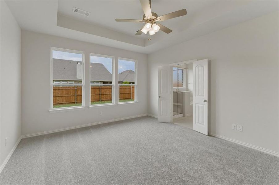 Spacious room featuring light gray carpeting, a tray ceiling with a mounted ceiling fan, and three large windows