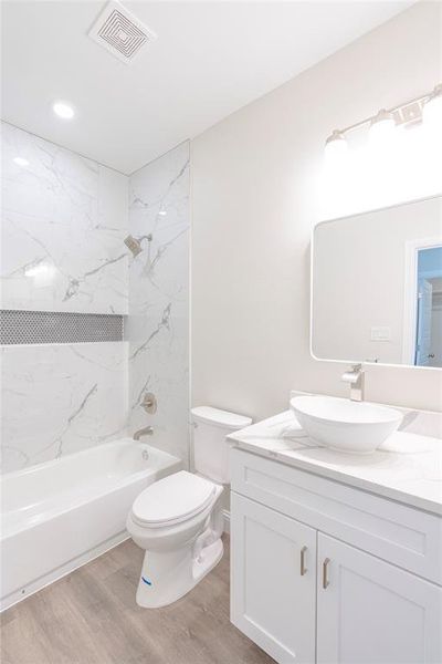 Full bathroom featuring hardwood / wood-style floors, tiled shower / bath, toilet, and vanity