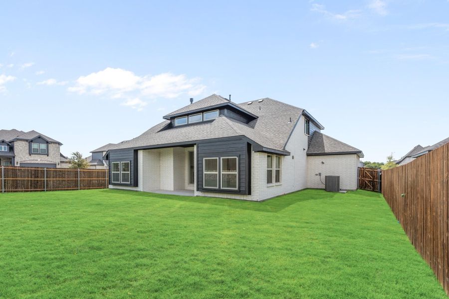 Rear view of two-story home with white brick, dark trim, covered patio, and fenced backyard with green lawn