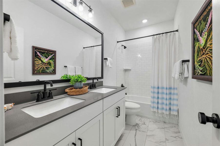 The full secondary bathroom is located upstairs alongside the secondary bedrooms and comes with a convenient dual vanity, Shaker-style cabinetry, stylish tile floors, and a shower/tub combo with subway tile backsplash.