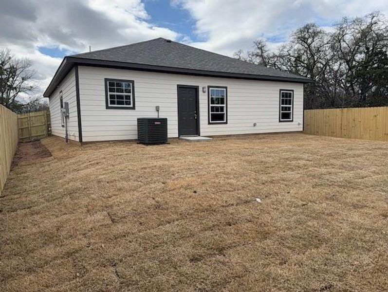 Back of house featuring a lawn, cooling unit, a fenced backyard, and roof with shingles