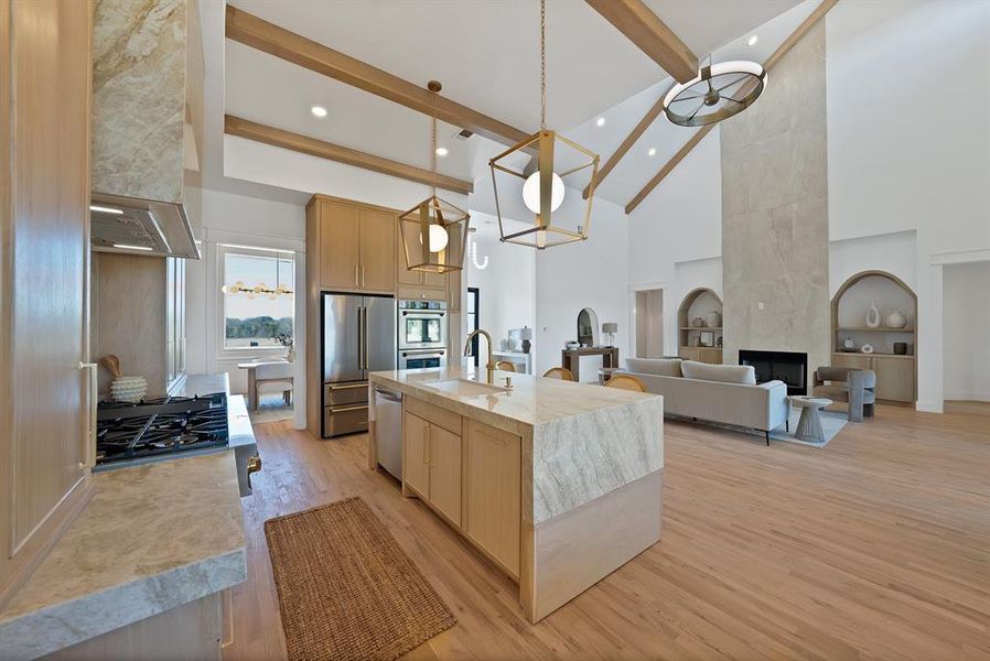 Kitchen with high vaulted ceiling, light brown cabinets, pendant lighting, appliances with stainless steel finishes, and light wood-style flooring
