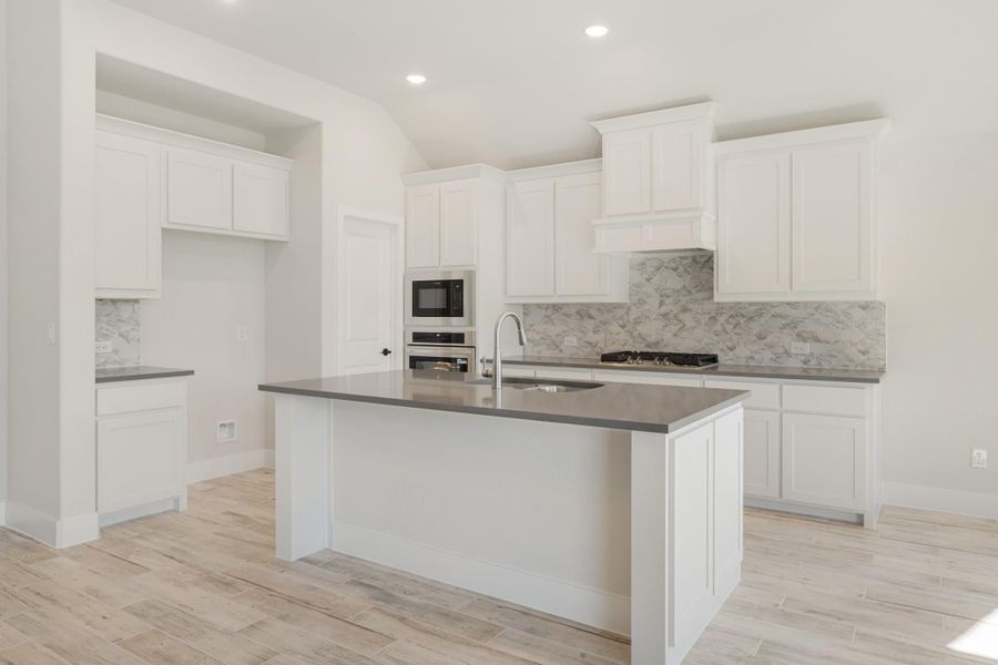 Kitchen with white cabinets, gray countertops, center island with sink, marble backsplash, and light wood floors Kitchen with white cabinets, gray countertops, center island with sink, marble backsplash, and light wood floors