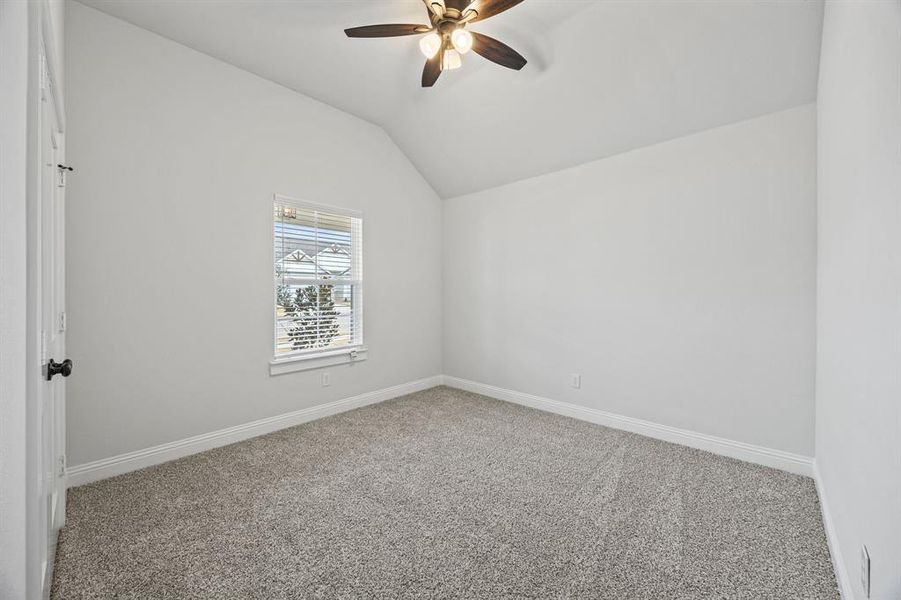 Empty room with carpet floors, vaulted ceiling, and ceiling fan
