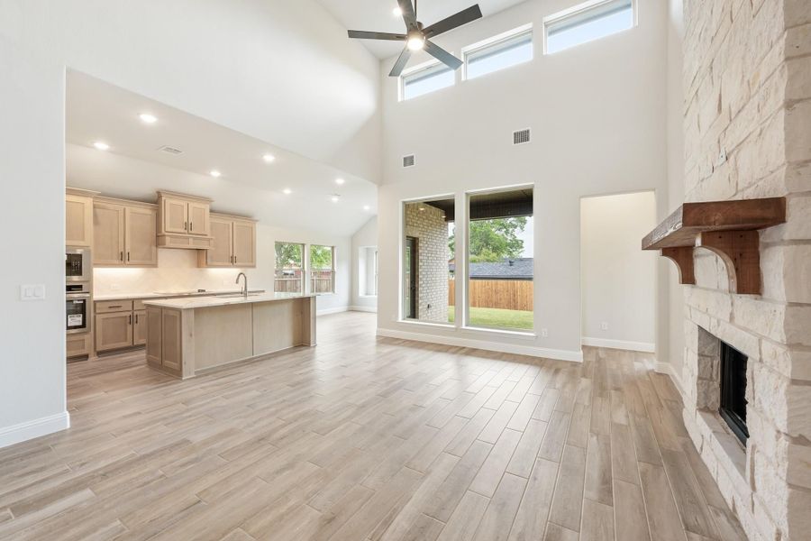 Open living area with vaulted ceiling, stone fireplace, and kitchen with island and wood-look floors