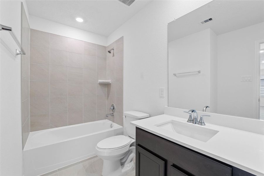 The secondary bathroom showcases tile flooring, a bath/shower combo with Daltile tile surround, a vanity with knee space and stunning light countertop, a mirror, sleek fixtures, and contemporary finishes throughout. The secondary bathroom showcases tile flooring, a bath/shower combo with Daltile tile surround, a vanity with knee space and stunning light countertop, a mirror, sleek fixtures, and contemporary finishes throughout.