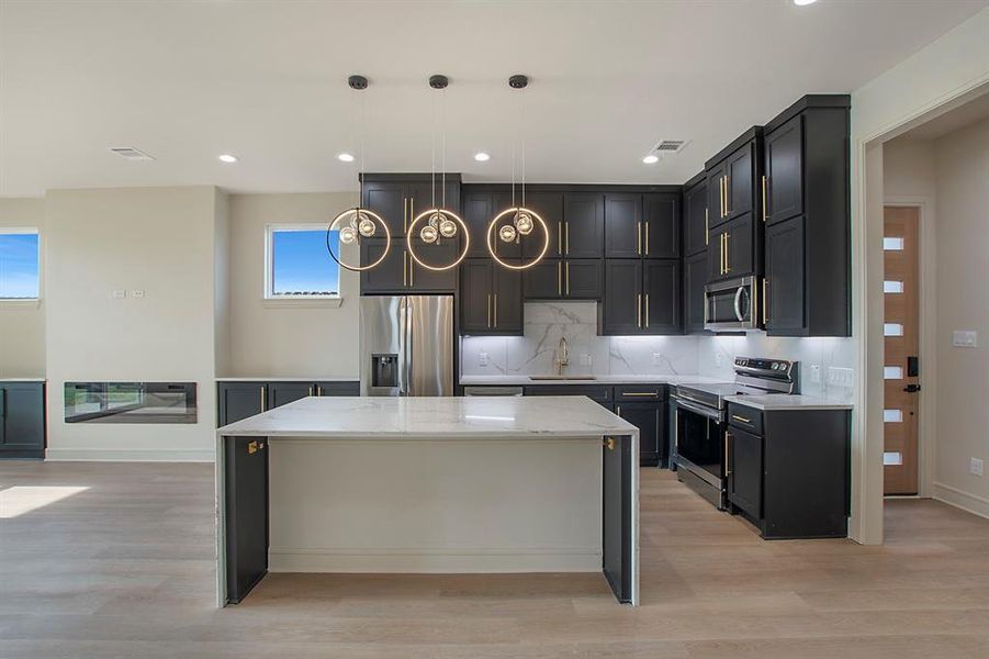 Kitchen with pendant lighting, stainless steel appliances, a kitchen island, and a healthy amount of sunlight