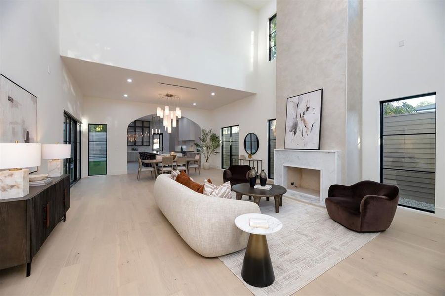 Living area featuring light wood-type flooring, a chandelier, a premium fireplace, a towering ceiling, and arched walkways