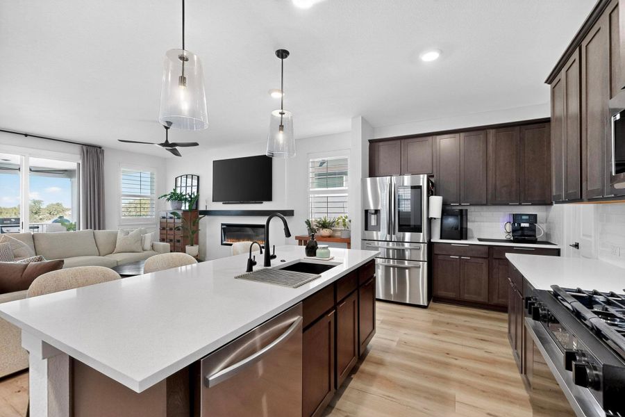 Kitchen featuring espresso cabinetry, stainless steel appliances, open floor plan, decorative light fixtures, and recessed lighting