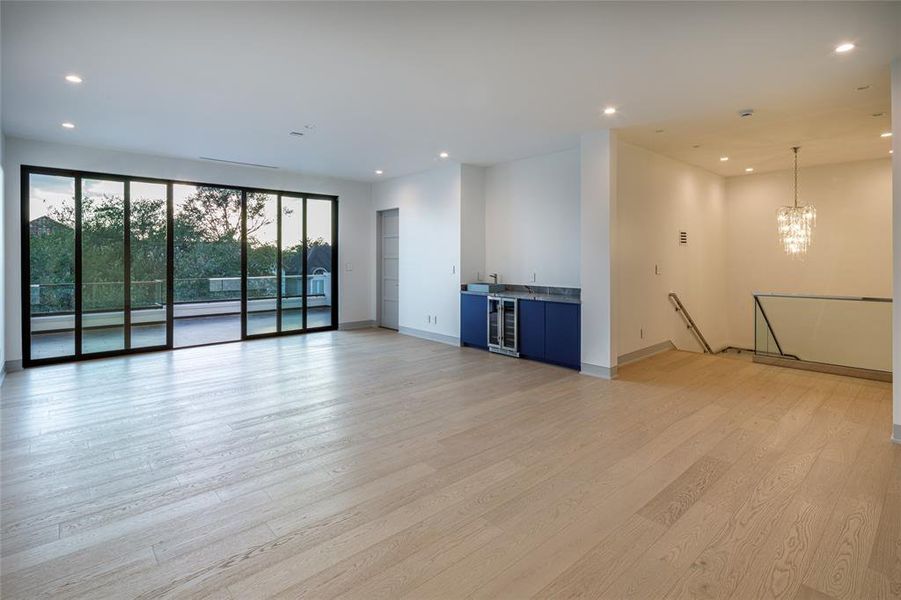 Stair-case with glass railing leads to the third floor light filled oversized game room with built-in wet bar, wine chiller, wide-plank wood floors and wall of glass and steel sliding doors transitioning to the outdoor door private terrace