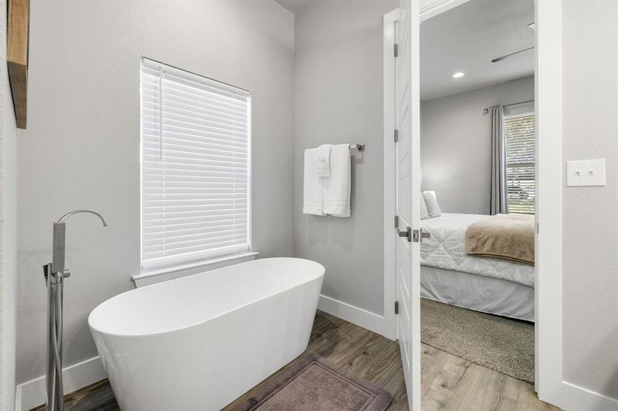 Ensuite bathroom featuring wood finished floors, a soaking tub, and a textured wall