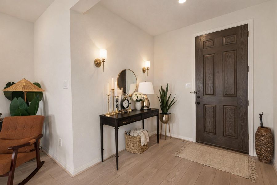 Bright entry foyer features upgraded light wood floors, modern wall sconces, and a dramatic stained front door.