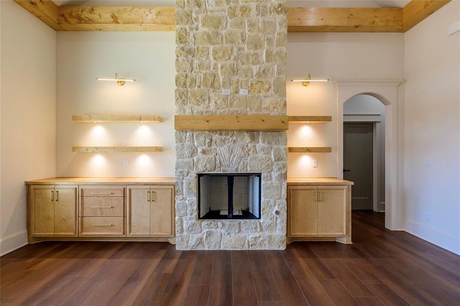 Unfurnished living room with a stone fireplace, beam ceiling, dark wood finished floors, and arched walkways Unfurnished living room with a stone fireplace, beam ceiling, dark wood finished floors, and arched walkways