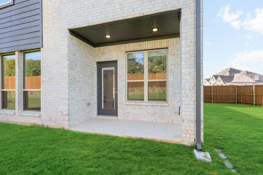 Back exterior of home with light brick, covered patio, dark door, and fenced green backyard