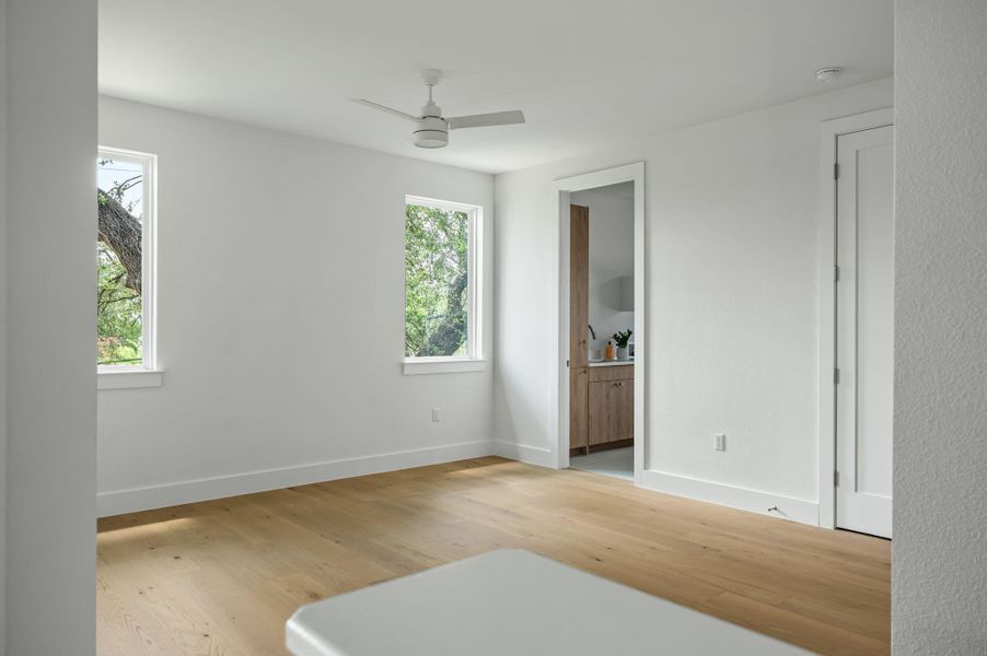 Blonde hardwood flooring brightens this spacious room, featuring a modern ceiling fan and verdant outdoor views. Blonde hardwood flooring brightens this spacious room, featuring a modern ceiling fan and verdant outdoor views.