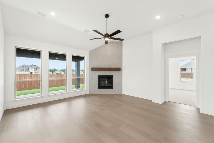 Open living room with vaulted ceiling, tile fireplace, ceiling fan, and hardwood floors Open living room with vaulted ceiling, tile fireplace, ceiling fan, and hardwood floors