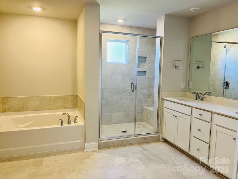 Primary bath featuring a soaking tub, tiled shower and double vanity with quartz countertops