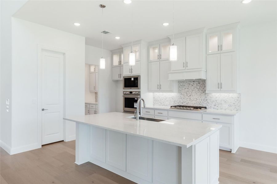 White kitchen with large island, quartz countertops, double wall ovens, and pendant lights over hardwood floors