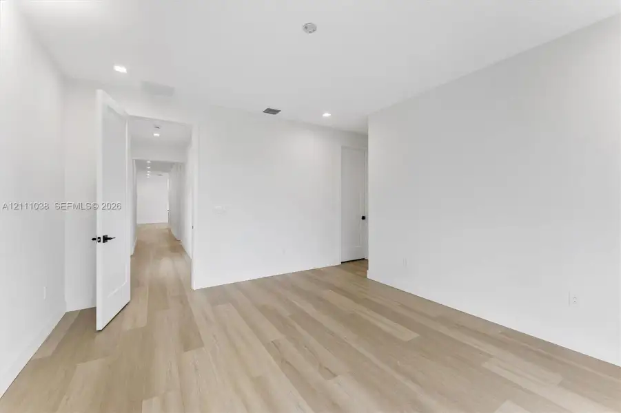 Neutral interior space featuring wood-finish flooring, recessed lighting, and solid-core doors with matte black hardware
