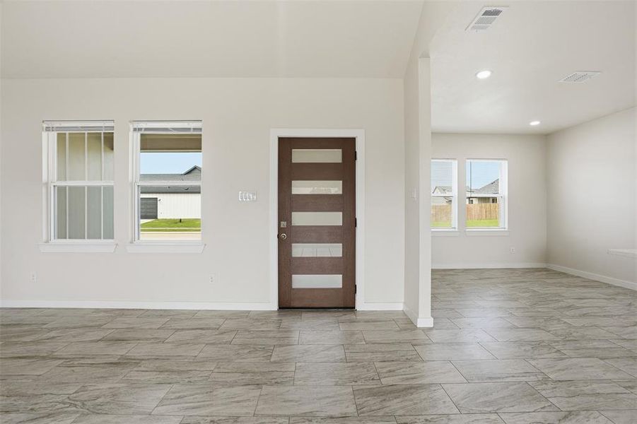 Spacious entryway featuring a modern wood-finish door with frosted glass inserts, light gray tile flooring, recessed lighting, and white walls