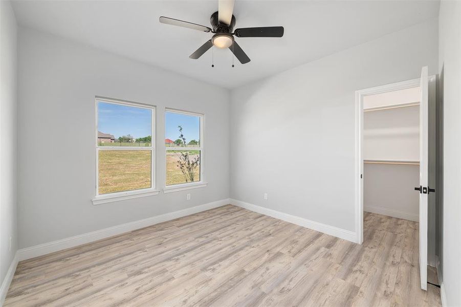 Unfurnished bedroom with a walk in closet, baseboards, light wood-style floors, and a closet