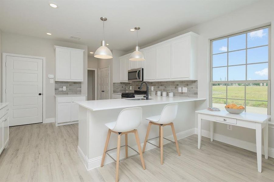 Kitchen with light countertops, a kitchen bar, stainless steel microwave, a peninsula, and light wood-style floors