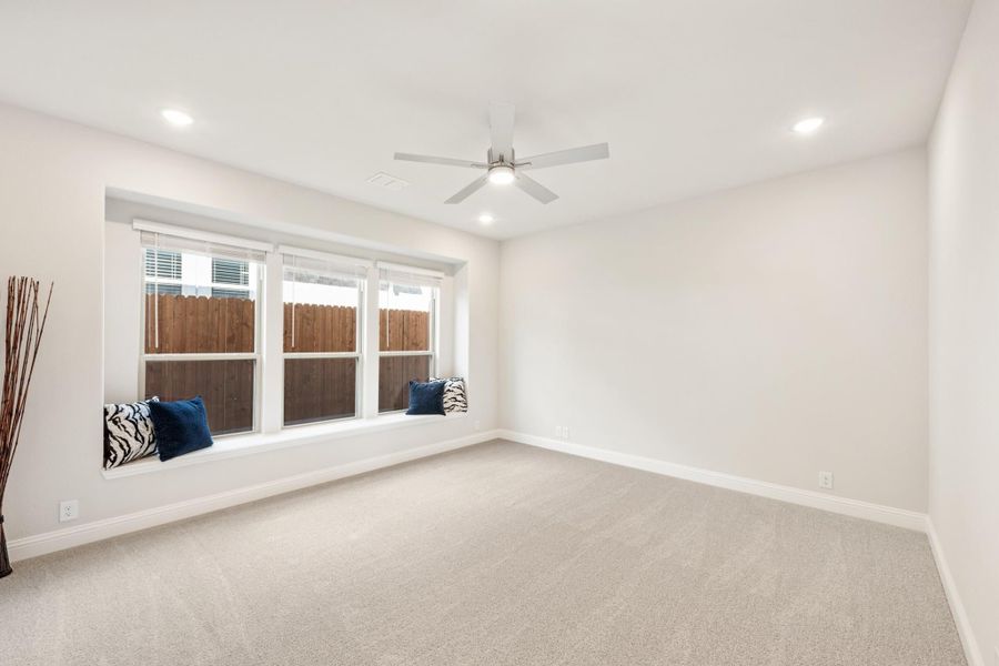 Empty bedroom with carpet, ceiling fan, and built-in window seat with decorative pillows