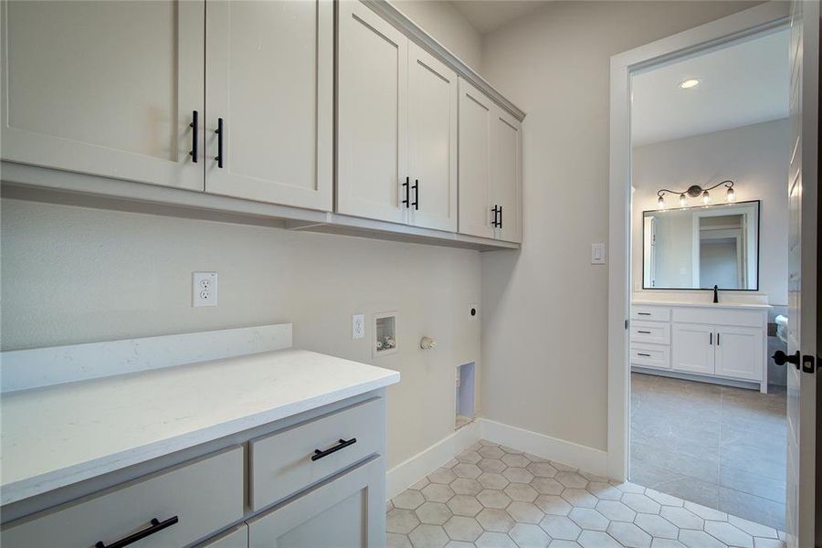 Washroom featuring cabinets, electric dryer hookup, washer hookup, sink, and light tile floors