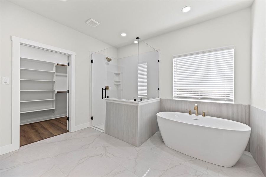 Full bath with light marble finish flooring, a walk in closet, a freestanding tub, recessed lighting, and a shower stall Full bath with light marble finish flooring, a walk in closet, a freestanding tub, recessed lighting, and a shower stall
