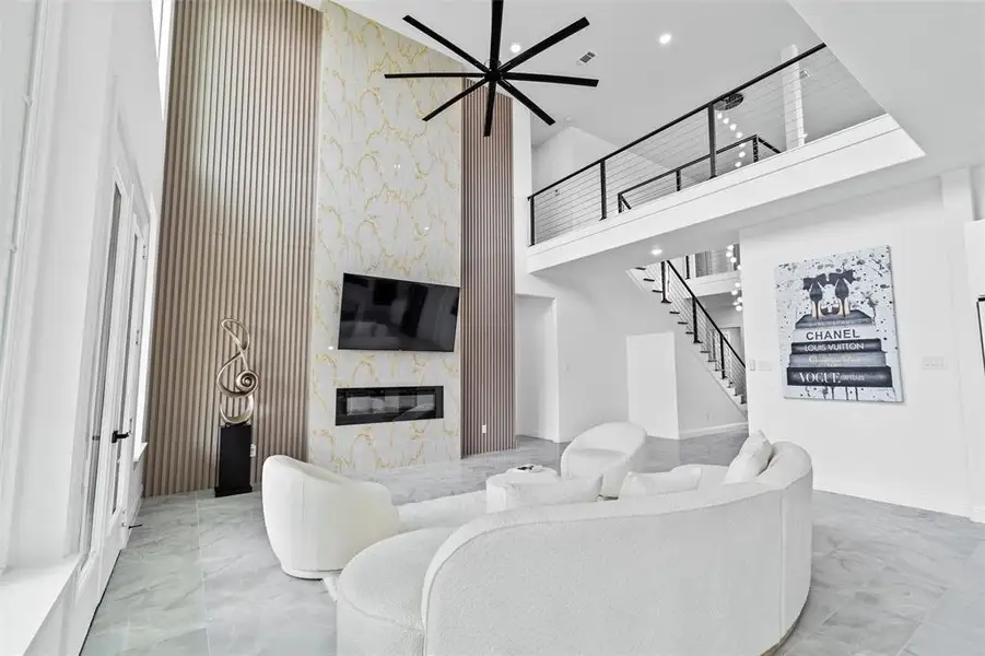 Two-story living area featuring a prominent fireplace wall with a linear electric fireplace, contrasting vertical wood paneling, and a large format marble-look accent wall