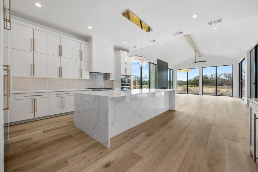 Kitchen featuring white cabinets, hanging light fixtures, beamed ceiling, a center island with sink, and decorative backsplash