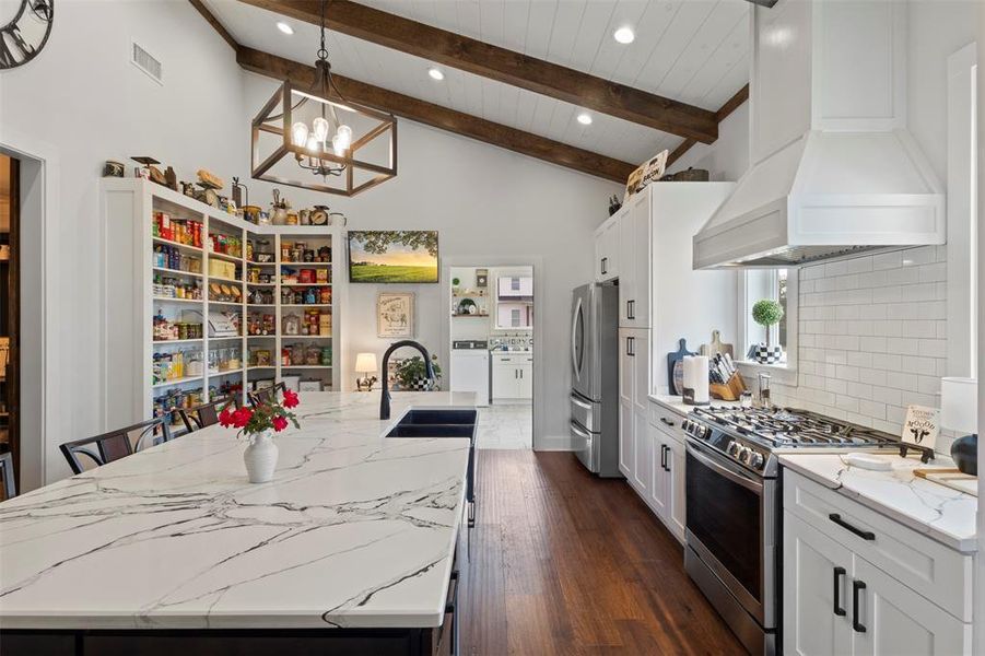 Expansive farmhouse-style kitchen featuring soaring beamed ceilings, a statement island with quartz countertops, and a gas range with convection oven—designed for both everyday cooking and effortless entertaining.
