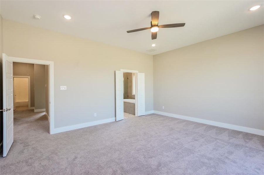 Unfurnished bedroom with ceiling fan, light colored carpet, and connected bathroom