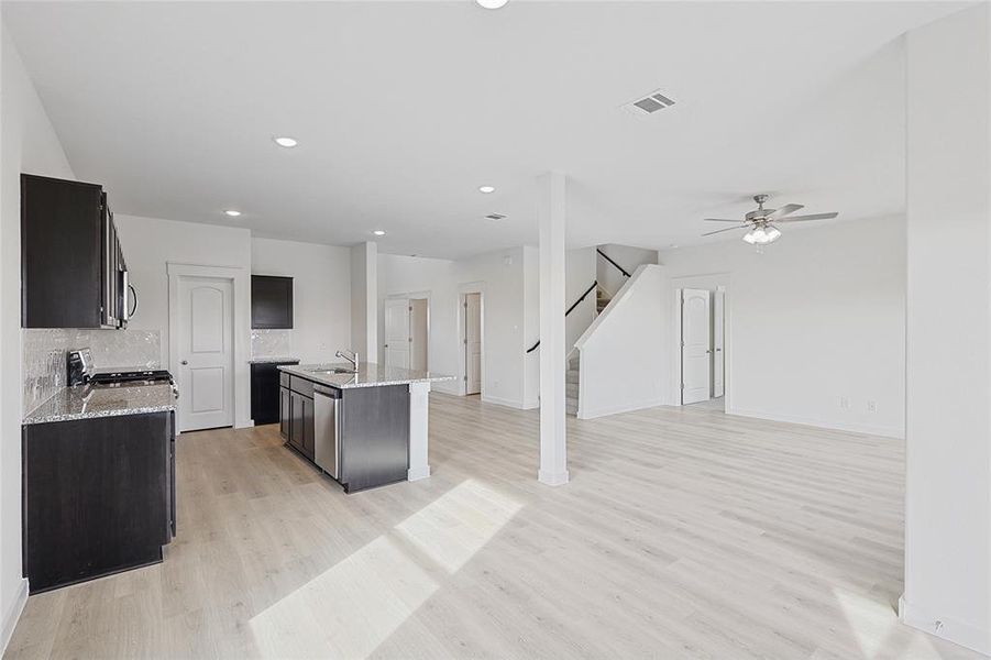 Kitchen with ceiling fan, stove, decorative backsplash, a center island with sink, and light wood-type flooring